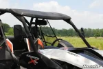 Side view mirror mounted to the cage of a Can-Am Maverick with a roof, parked in a grassy field