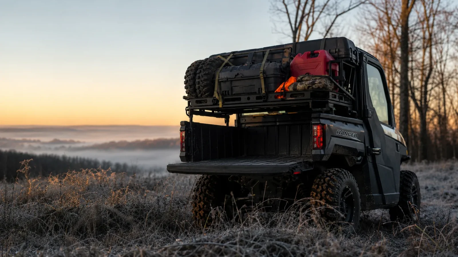 A Polaris Ranger hunting rig with a loaded cargo rack, spare tire, fuel can and blaze-orange gear at frosty dawn