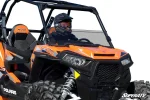 Rider in a helmet behind a tinted half windshield clamped to the cage of an orange and black Polaris RZR