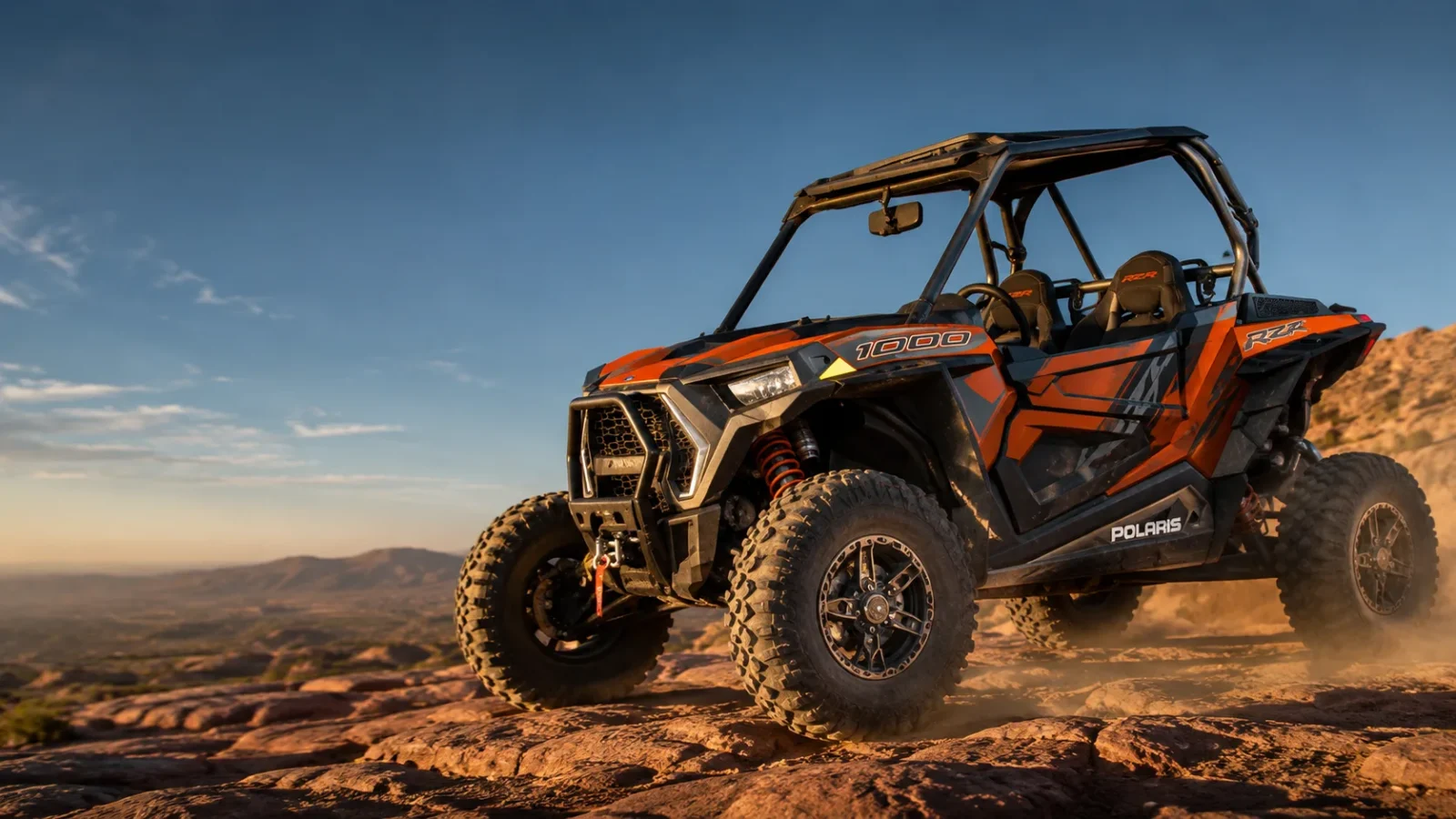 Polaris RZR XP 1000 climbing a rocky desert ridge at sunset