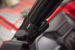 Close-up of Tusk mirror arm clamped to a black roll cage tube, TUSK logo on the mount