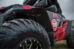 Close-up of a black rear fender flare installed above a muddy tire on a red Polaris RZR